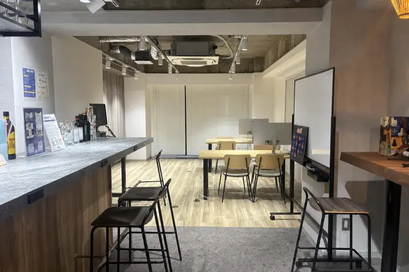 昼のWorkspace & Bar 56の実際の店内。手前にバーカウンターとハイチェア、奥にテーブル席とホワイトボードのあるワークスペースが広がる様子